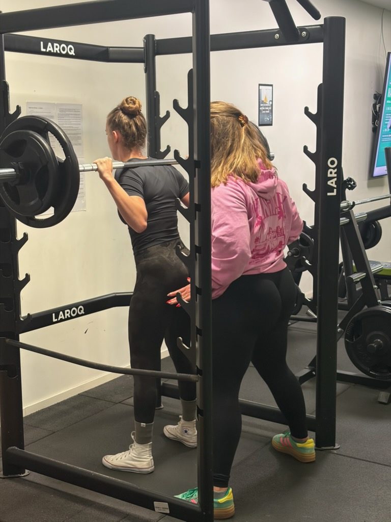 Lara corrige la posture d'une cliente au squat